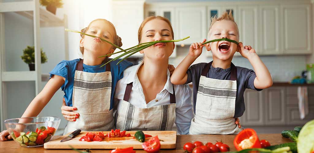 kids and mom in kitchen playing with vegetable mustaches.