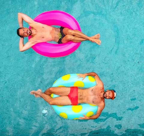 above 2 guys floating in blow up rings in blue pool.