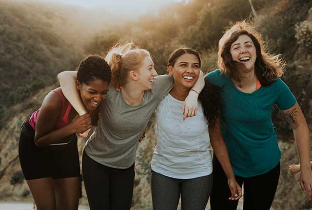 four women laughing while walking a desert trail.