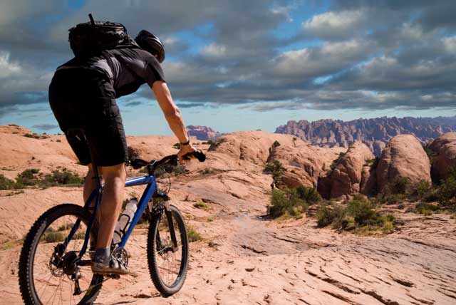 guy riding bike into desert with mountains in the distance.