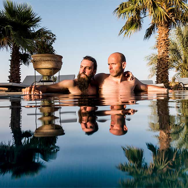 gay male couple in pool looking towards sunset.
