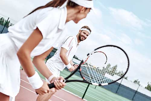couple on the tennis court holding rackets.