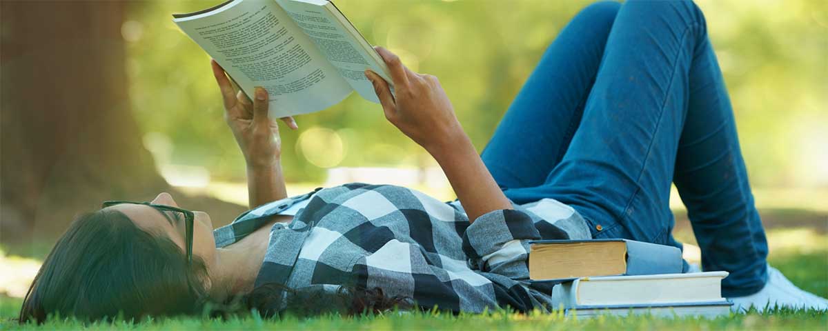 woman laying on grass reading a book.