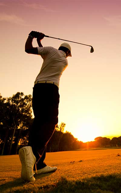 golfer swinging with sun setting in distance.