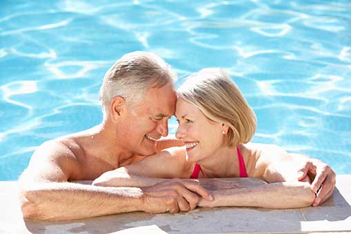 senior couple in pool at edge smiling at each other.